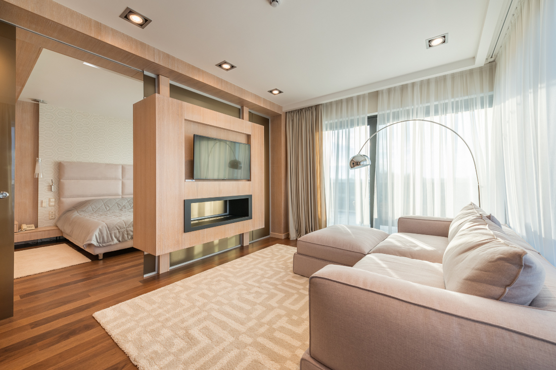 Wide beautiful room featuring a beige corduroy couch and large windows letting in natural light